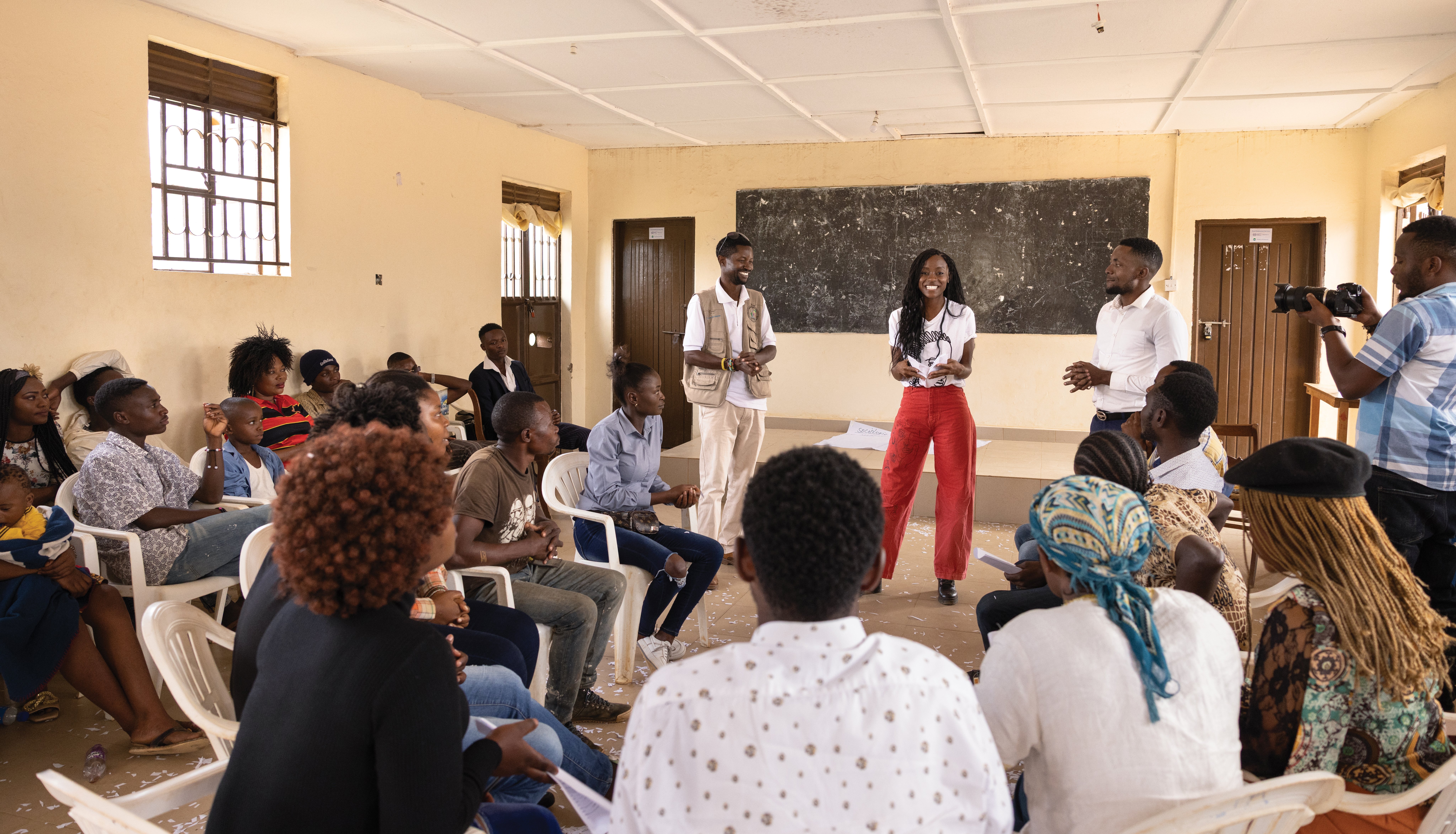 Sibongile Mlambo and people People seated in a community meeting while speakers present at the front of a classroom at the visits the World Refugee Film Academy.