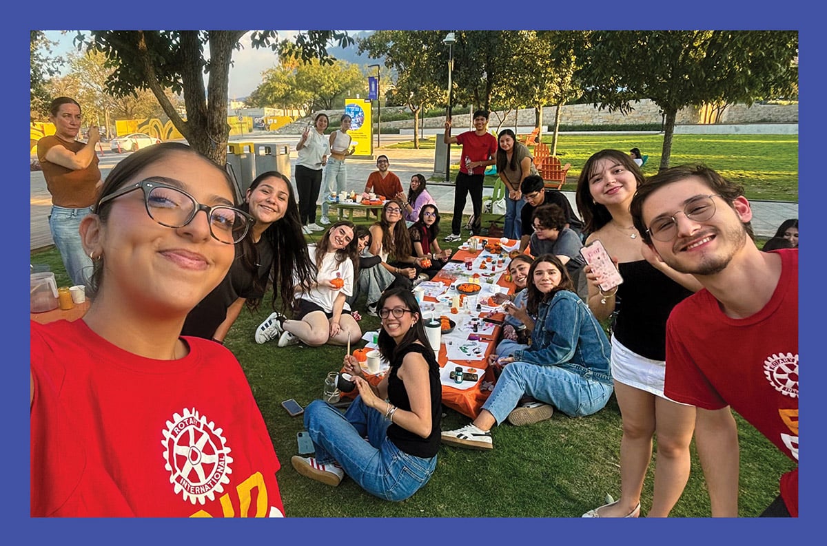 Students at Universidad de Monterrey in Mexico gathered on a picnic blanket outdoors, taking a group selfie in a park.