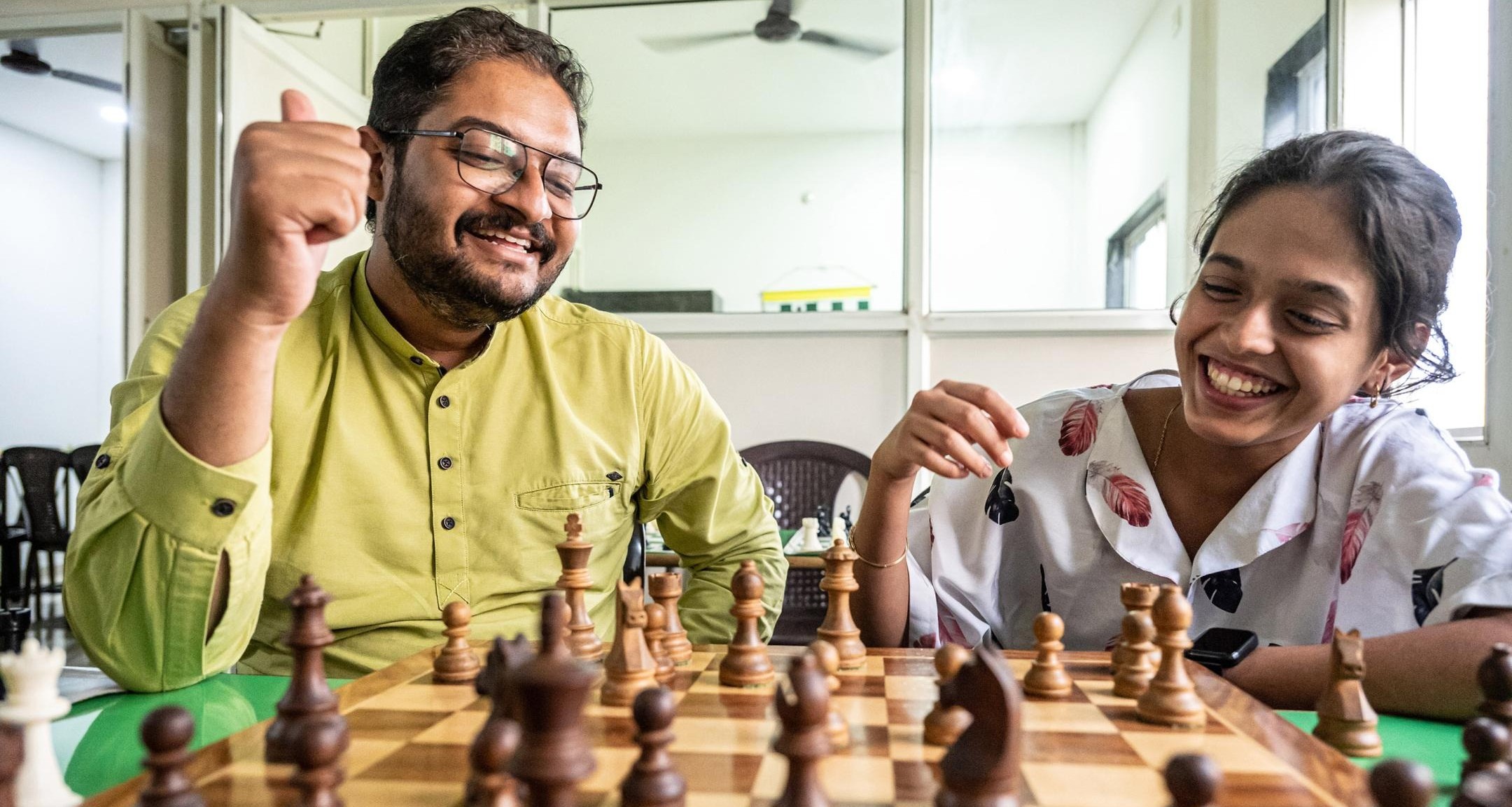 Person and child playing chess across a table with chess pieces arranged on the board.