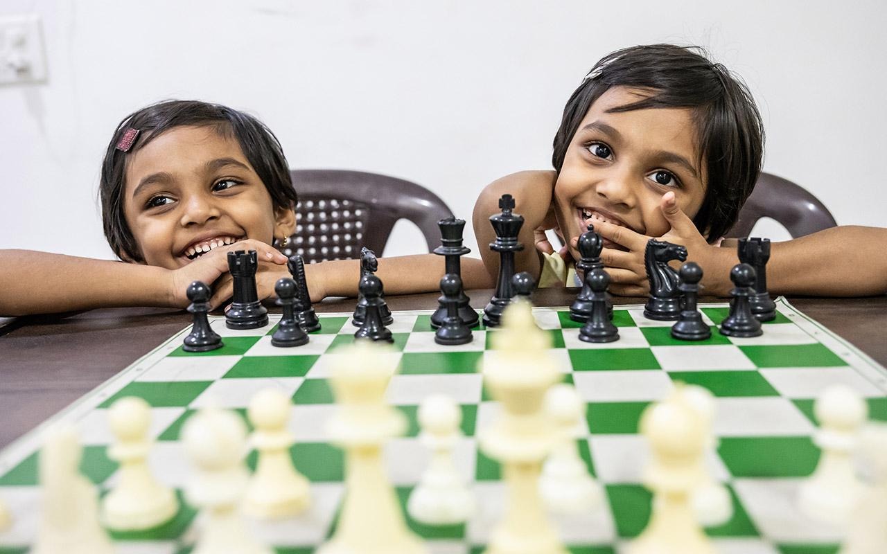 Person and child playing chess across a table with chess pieces arranged on the board.