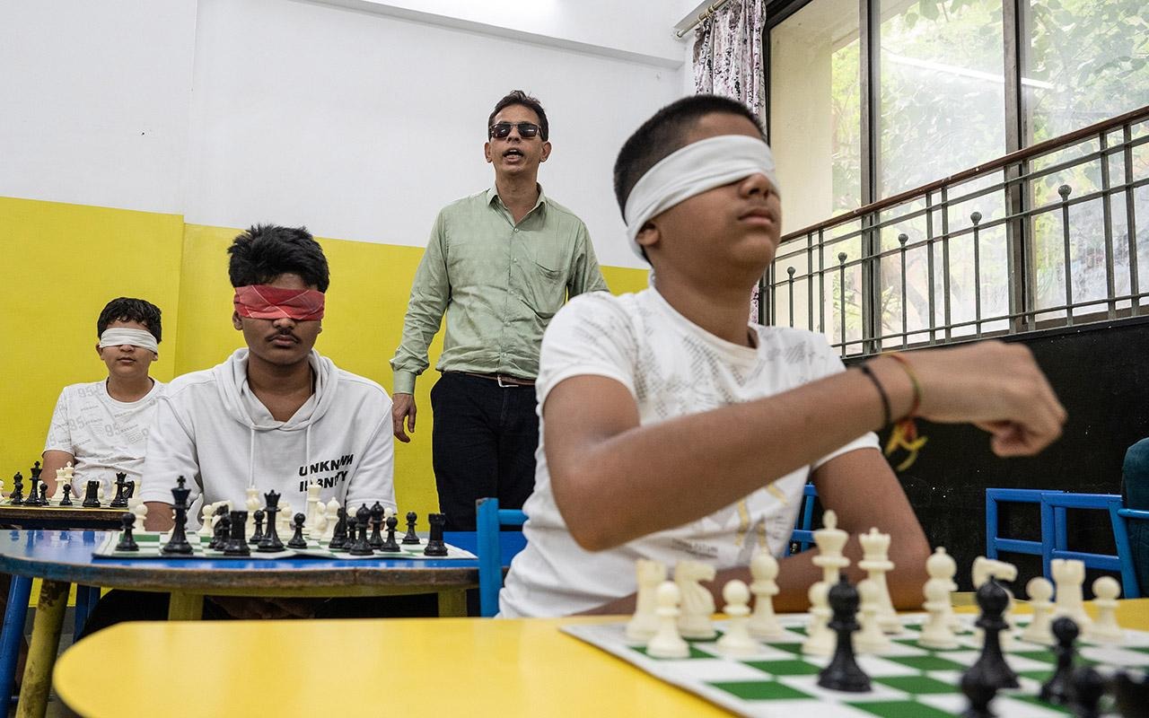 Participant wearing a blindfold moving a chess piece during a chess activity while others observe nearby.