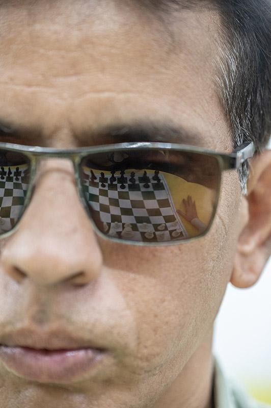 Chessboard reflected in sunglasses worn by a person looking toward the game.