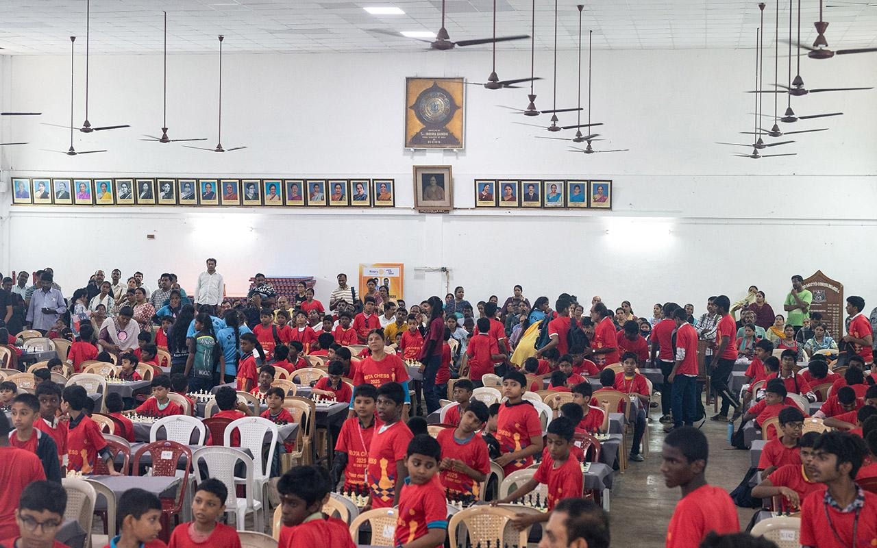 Large group seated at tables in a hall participating in a chess event with multiple chessboards.