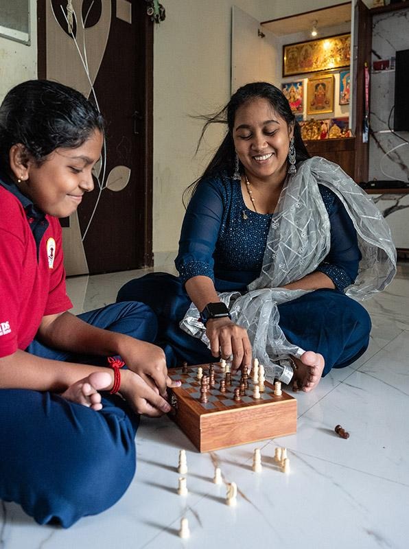 Two people stacking wooden blocks on a table while seated on the floor indoors.