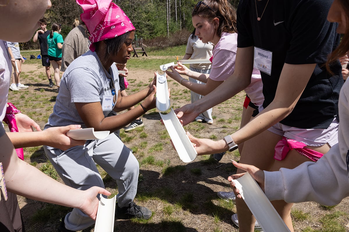 In a team-building activity, participants work together to roll a ball down sections of PVC pipe. 