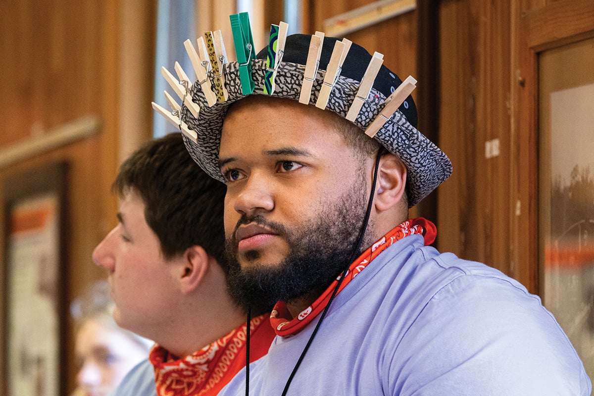 A counselor models a hat studded with clothespins, which were placed on people’s clothes to remind them to check for ticks.  