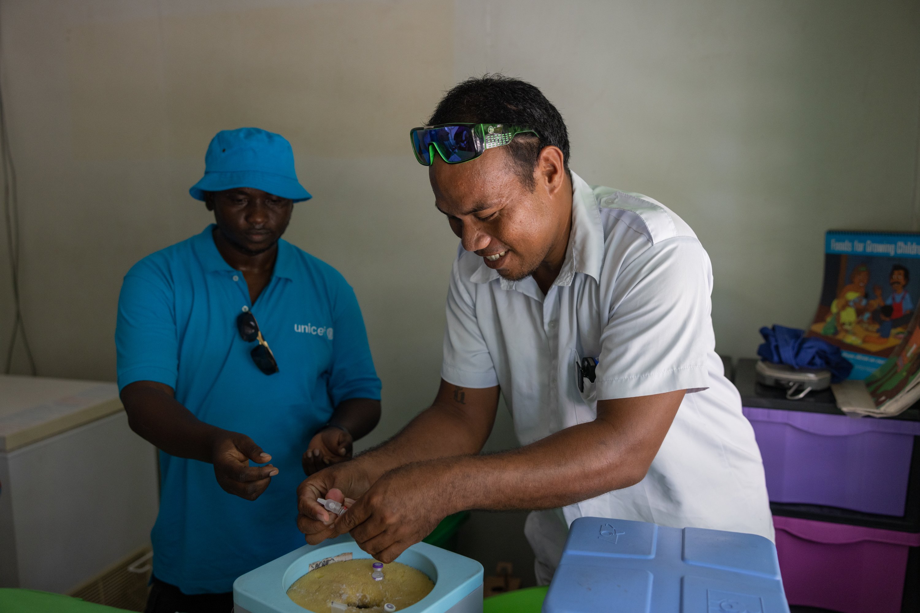 Two healthcare workers prepare a syringe to vaccinate a child inside a community health clinic.