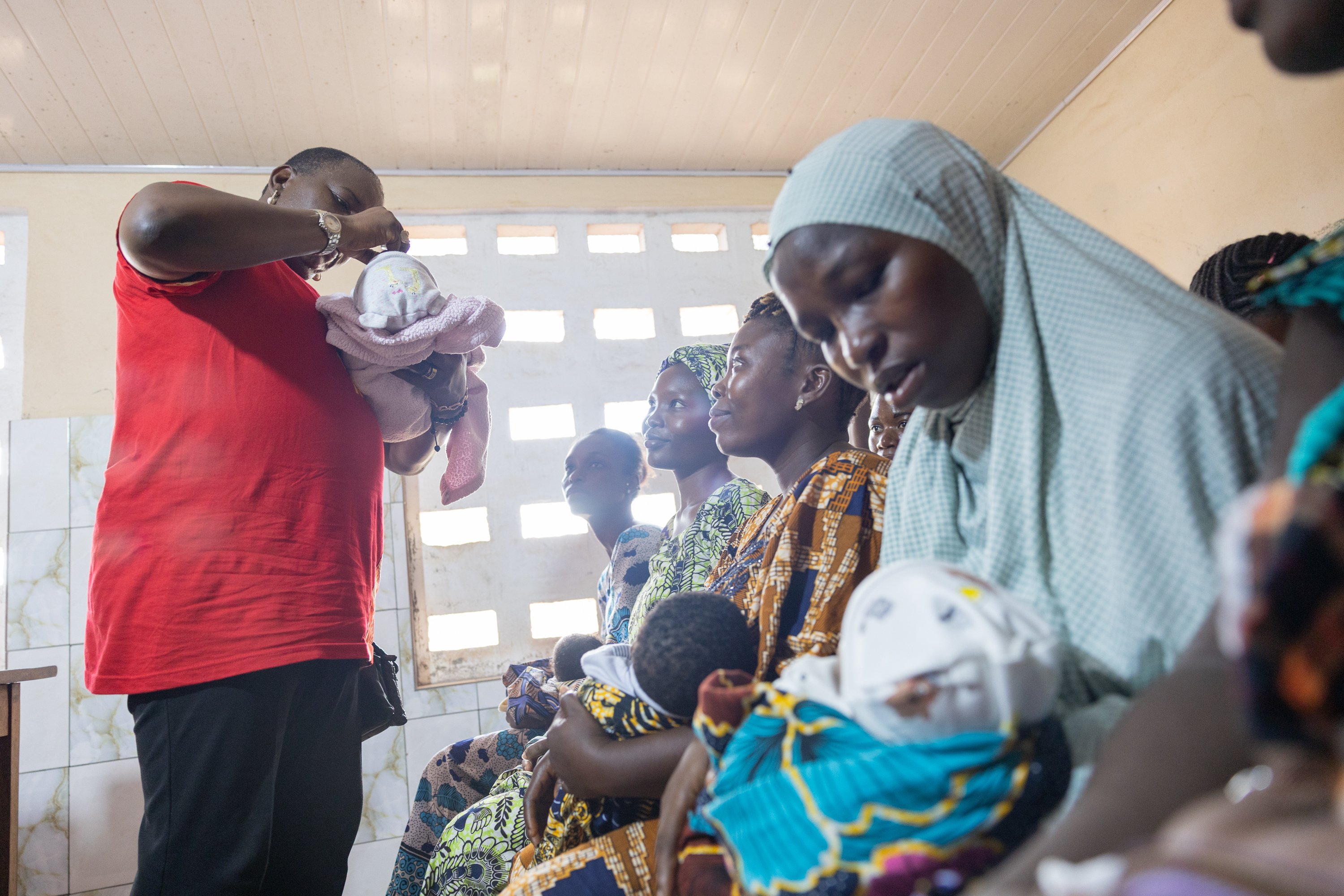 Health worker administers a vaccine to a child as caregivers sit nearby at a clinic during a community health event.