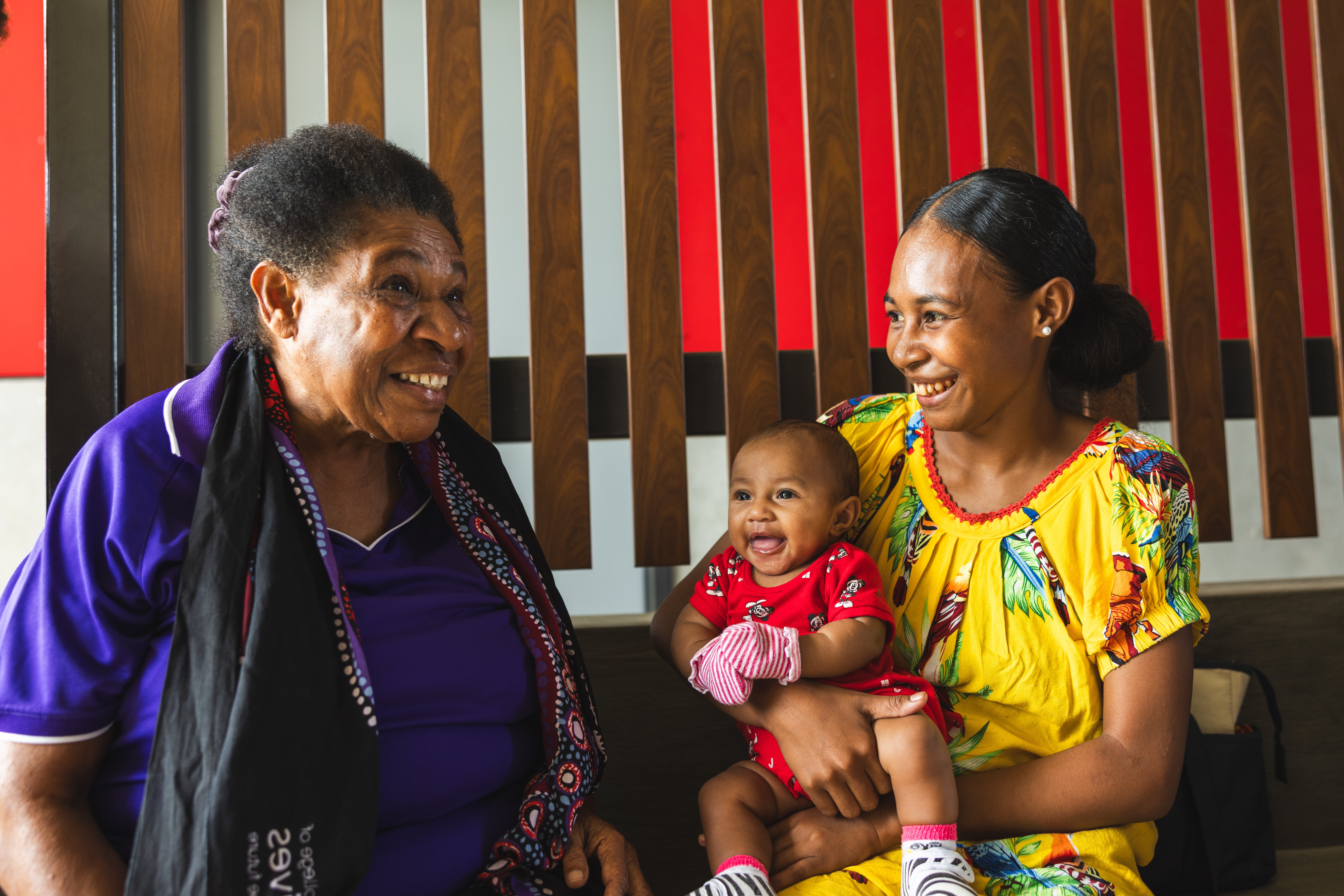 Healthcare worker speaks with a mother holding her child during a health consultation indoors.