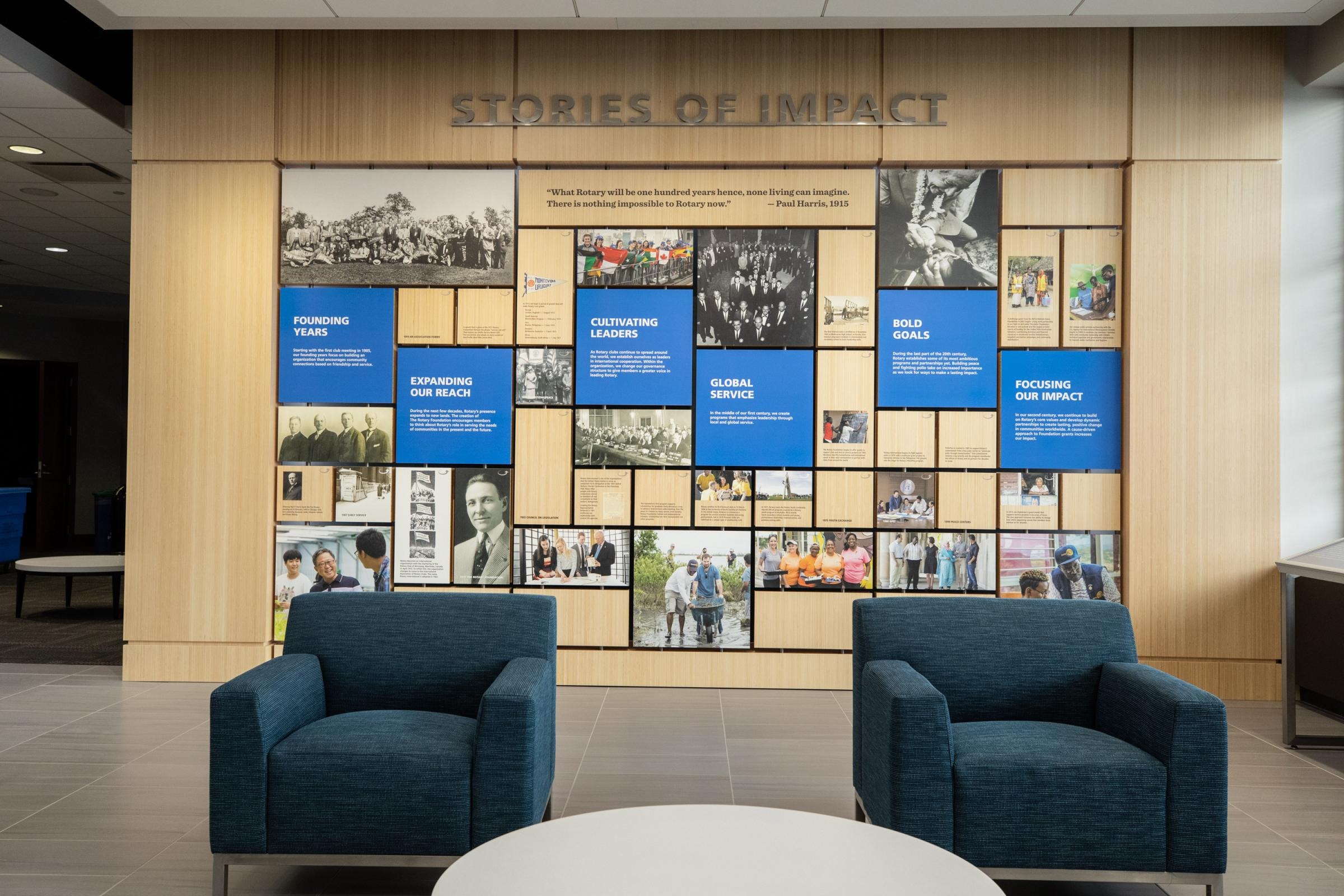 Two blue chairs sit in a lobby facing a wall display with photos and text panels.
