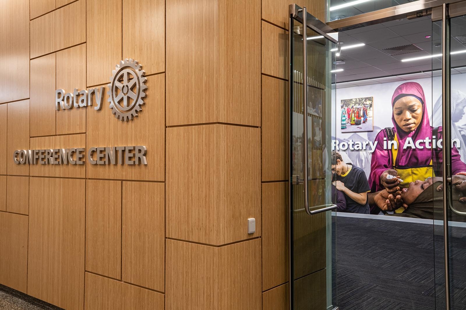 Wood wall with “Rotary International” signage beside a glass door displaying a poster of a person holding a child.