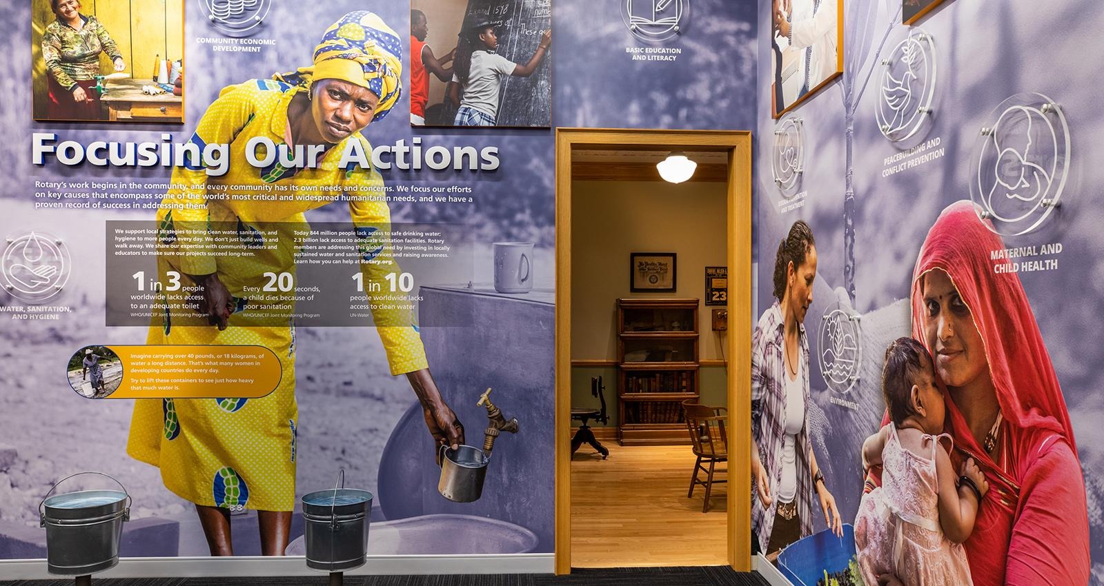 Wall mural with text “Focusing Our Actions,” showing health scenes beside an open doorway into an office space.