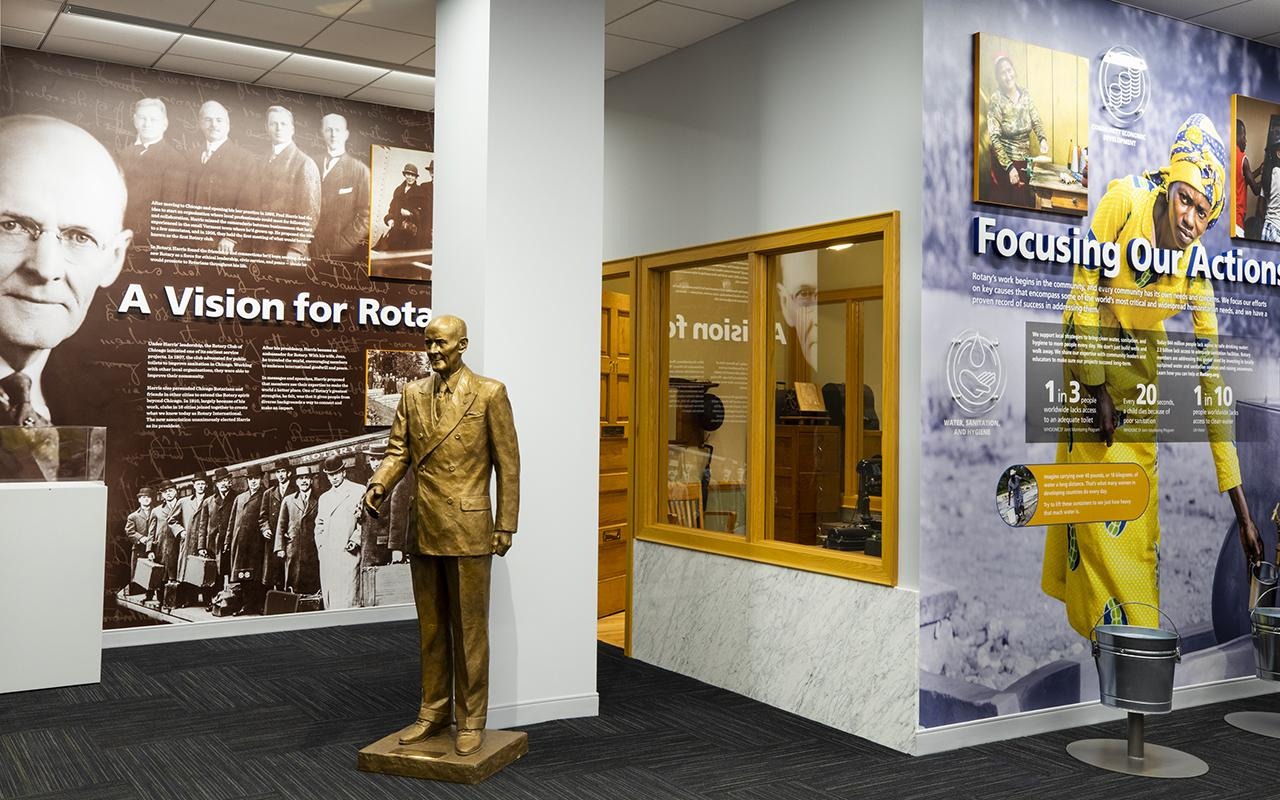 In un atrio, una statua di bronzo si trova accanto a dei pannelli appesi alla parete con le scritte “Una visione per il Rotary” e “Concentrare le nostre azioni”.