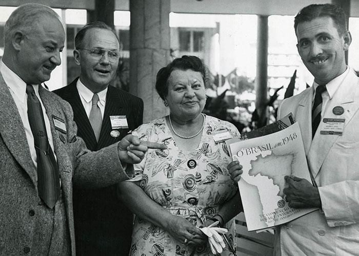 Four people stand together as one presents a certificate or document to another during an indoor event.