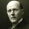 Portrait of Paul Harris, a man wearing glasses and a dark suit against a plain background.