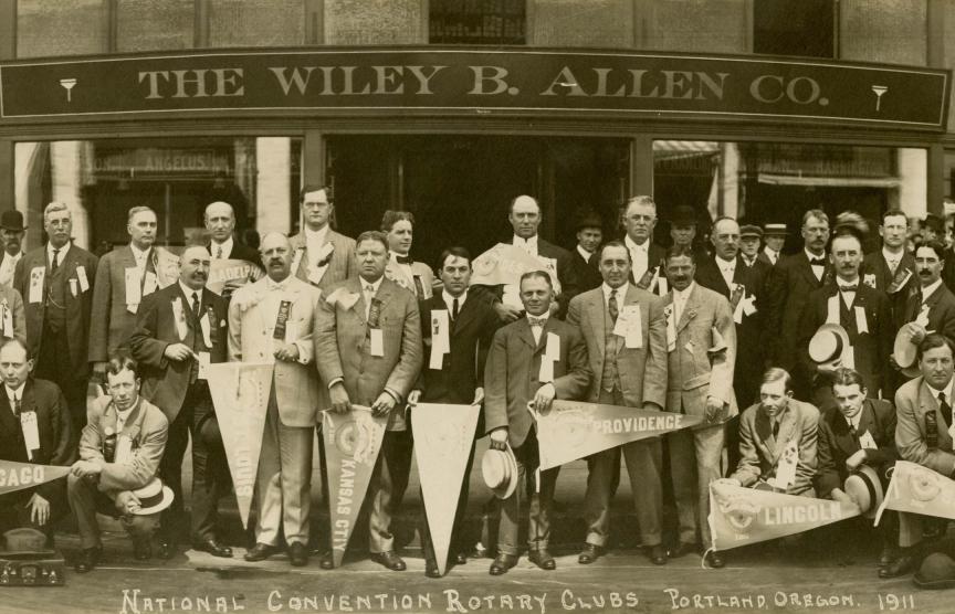 Large group of people pose together outside a storefront with “The Wiley B. Allen Co.” sign above the entrance.