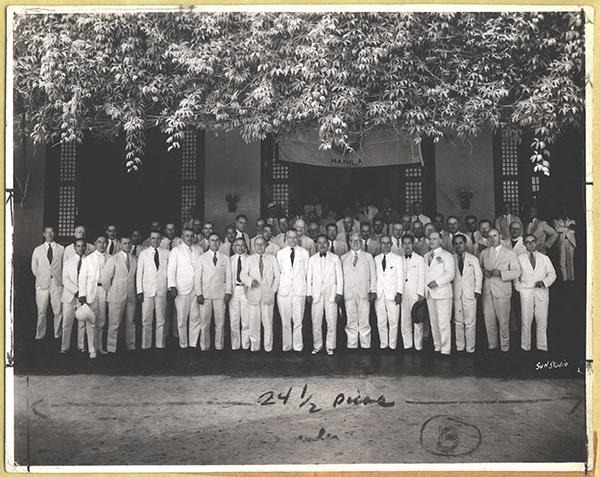 Un grand groupe de personnes se tient debout et assise en rangées devant un bâtiment, posant pour une photo de groupe.