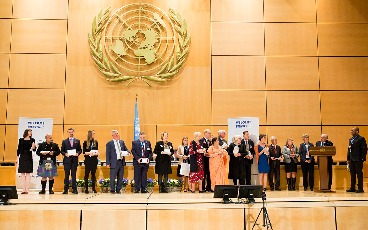 Eine Gruppe von Beamten steht auf einer Bühne bei den Vereinten Nationen, hinter ihnen ist das UN-Emblem deutlich sichtbar an der Wand angebracht.