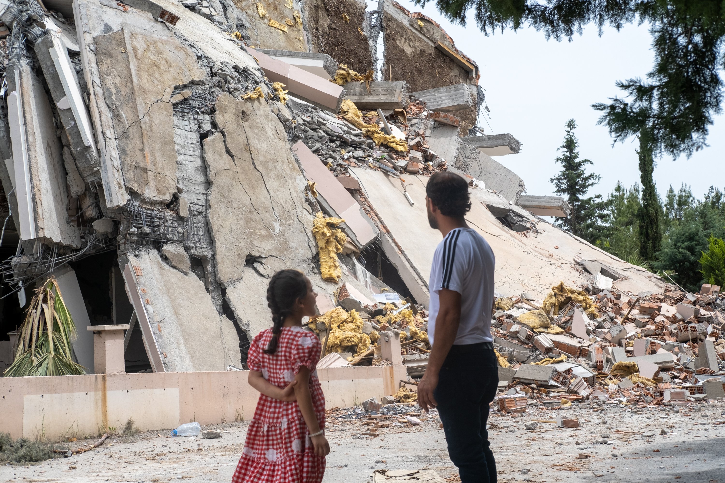 Two people stand near heavily damaged buildings in Gaziantep, Turkey, surveying destruction from the 2023 earthquake.