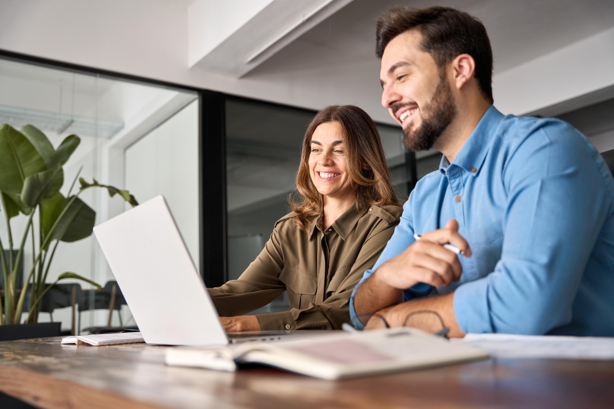 AdobeStock722373438 Two smiling professional business people talking using laptop computer working i