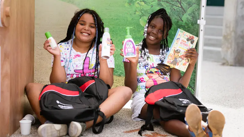 2 girls with distributed bottles of hand sanitizer and sunscreen and backpack