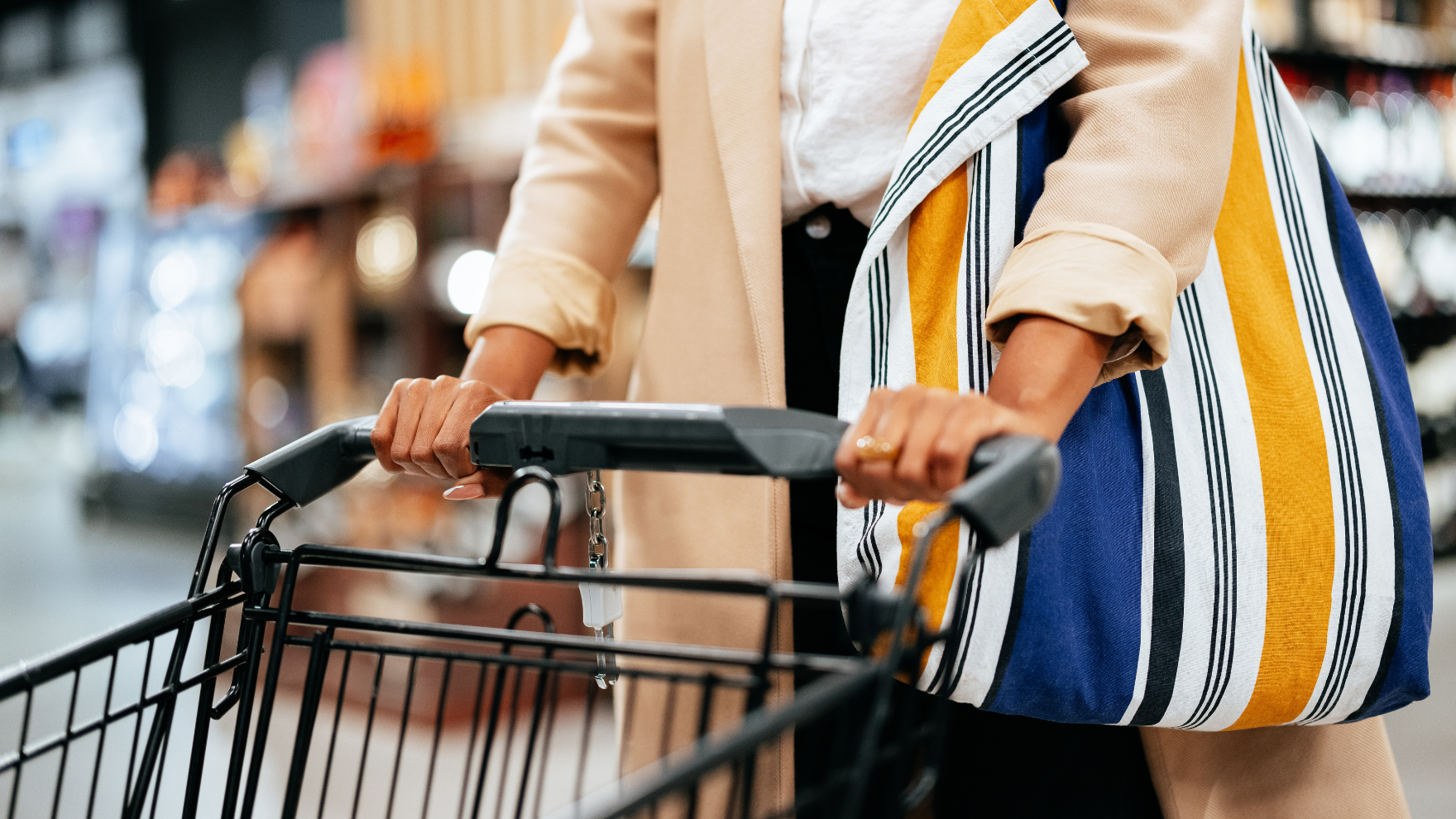 Person pushing a black shopping cart with both hands on the handle