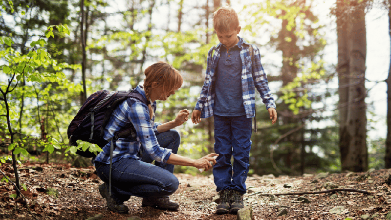 Adult applying bug spray to child in the woods