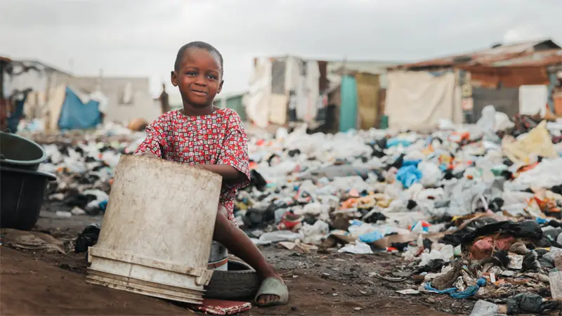 A child playing with plastic drum in garbage landfill.