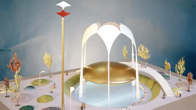 Futuristic pavilion rests on water, surrounded by miniature trees.