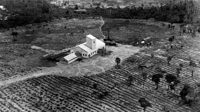 Building sits in cleared farmland amidst surrounding trees and fields.