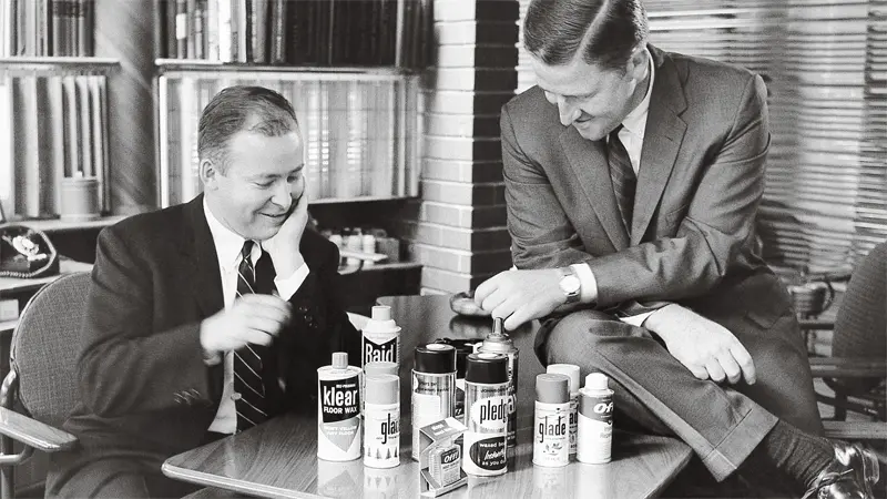 Two businessmen discussing products on a table, office background.