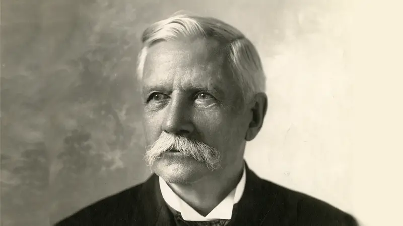 Man posing formally, wearing a suit, neutral background.