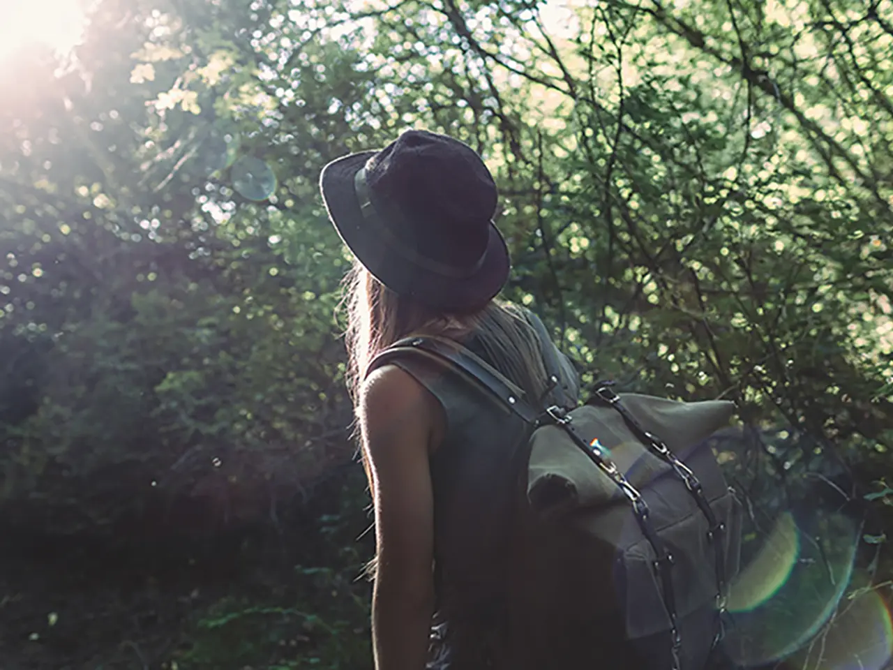 Femme entourée d’arbres, portant un sac à dos et faisant face à l’appareil photo