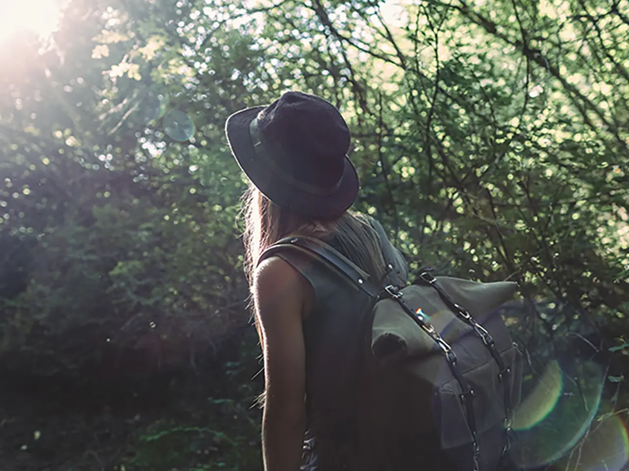Woman with a backpack surrounded by trees and facing away from the camera