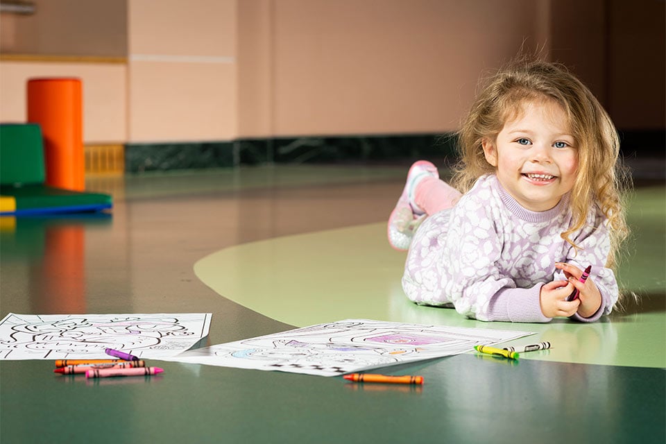 young girl laying on ground coloring