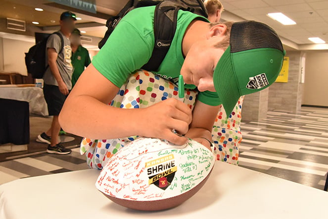 a child signing a football covered in signatures