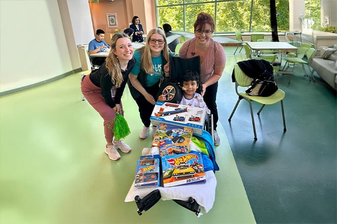 Carlitos con un surtido de juguetes Hot Wheels en su regazo frente a tres miembros del personal.