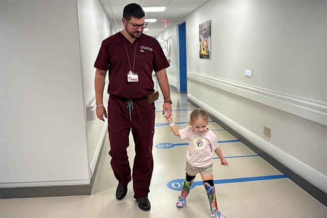 a young child with leg prosthetics walking with a healthcare provider