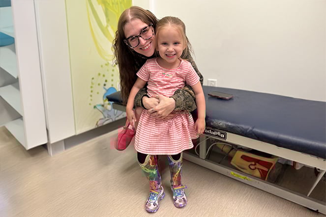 a young child with leg prosthetics being held by her mom