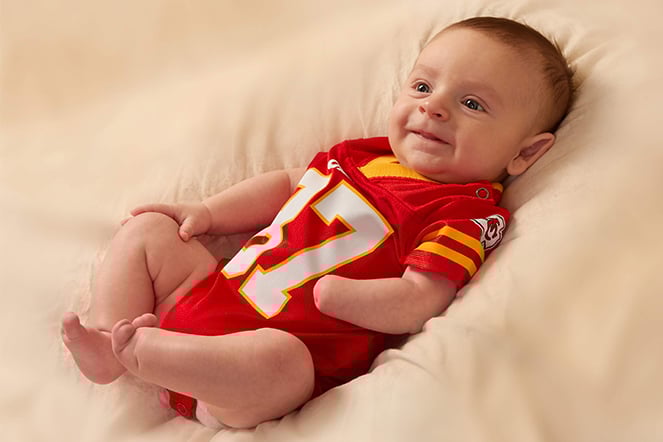 a smiling infant in a football jersey with limb differences on his left hand and foot