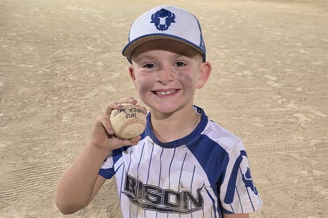a young baseball player holding up a ball that reads "game winning play"