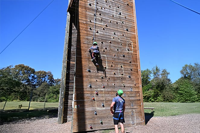 a child climbing up a rock wall while an instructor watches on