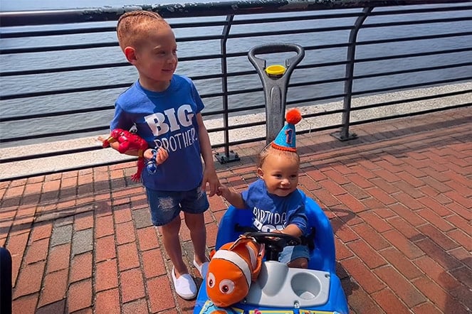 a young child smiling next to a toddler in a stroller