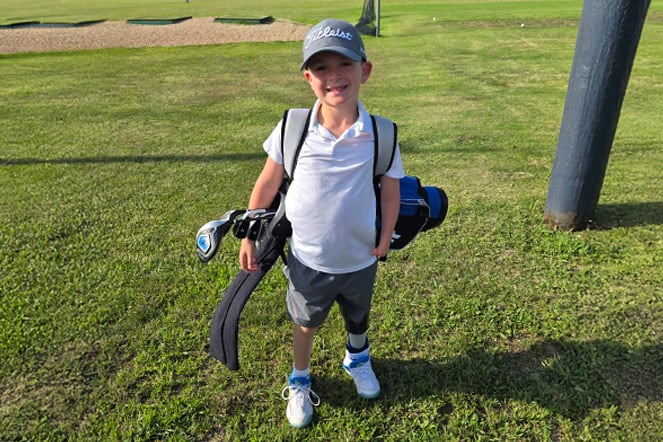 a young golfer with a limb difference stands at the driving range with his clubs