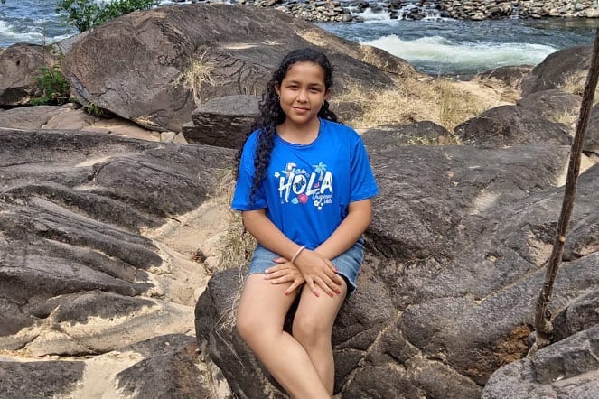 a teenager sitting on large rocks in front of a river