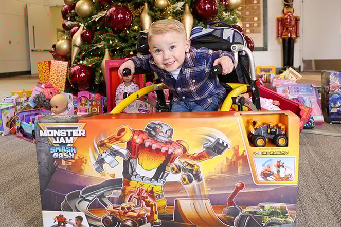 an excited child in a wheelchair smiling in front of a large box with the Monster Jam logo