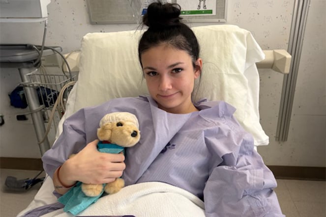 a smiling child in a hospital bed holding a plushie