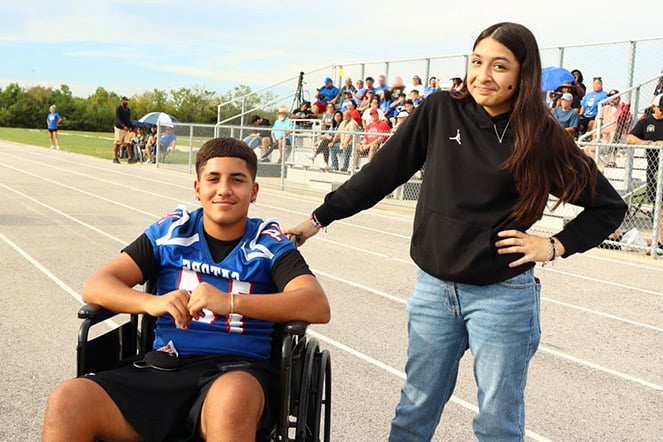 a child in a wheelchair next to another teenager at a football game