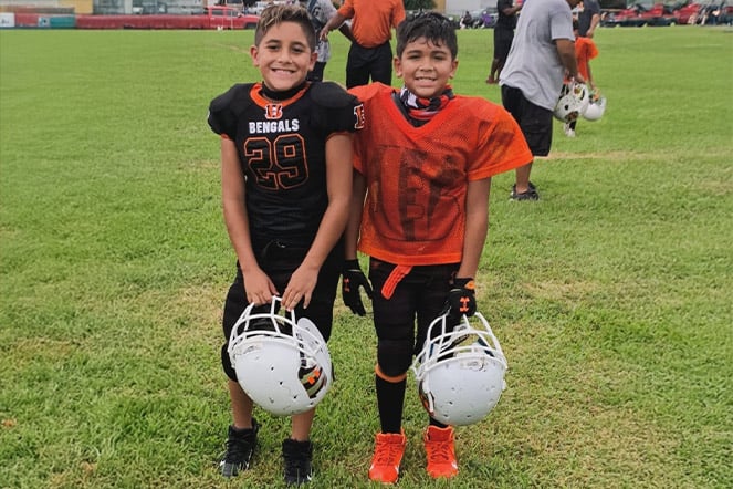 two young football players holding their helmets on a field