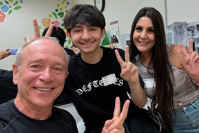 two adults and a teenager giving a peace sign